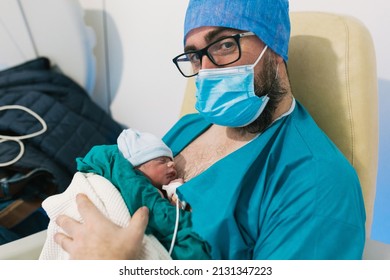 Man Wearing Face Mask While Holding His Newborn Baby In Hospital Room.