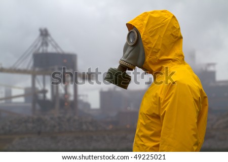 Man wearing gas mask standing infront of factory. Side shot. Background out of focus