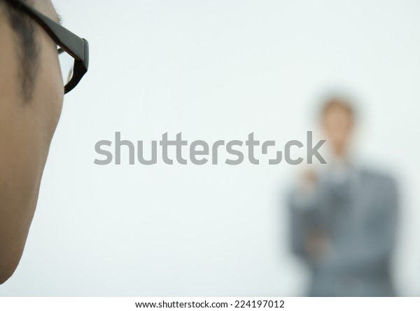Man wearing glasses, side of face, facing\
business man in blurred\
background