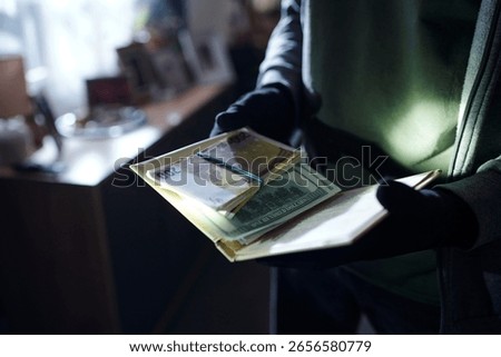 Man wearing gloves holding stack of euro and dollar banknotes in hands indoors, counting money with partial body visible, background out of focus