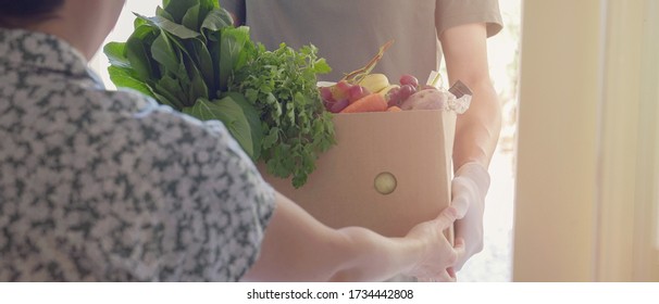 Man Wearing Gloves And Mask Home Delivering Or Collecting Food Box, Food Bank, Volunteer Holding Grocery Box For Donation Concept