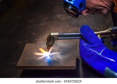 A Man Wearing Goggles And Gloves Is Heating A Sheet Of Metal With A Gas Cutter To Cut It Off.