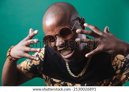 Man wearing gold teeth jewellery, also known as teeth grillsteeth slugs, photographed against a dark green background.