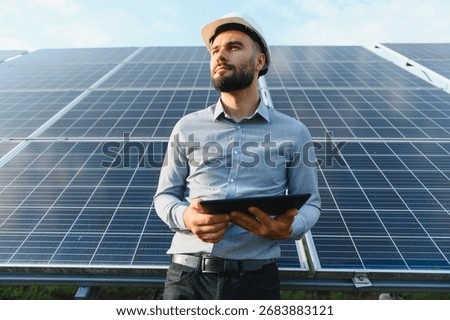 Man wearing hard hat checking solar photovoltaic farm data with digital tablet, promoting clean renewable energy