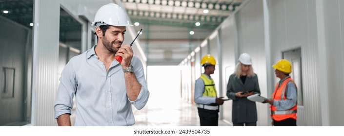 A man wearing a hard hat and a white shirt is talking on a cell phone. He is surrounded by other people, some of whom are wearing hard hats - Powered by Shutterstock