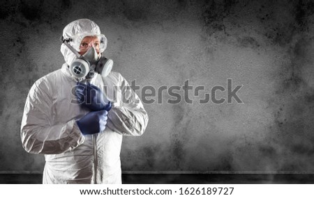 Man Wearing Hazmat Suit, Protective Gas Mask and Goggles Against Dark Wall.