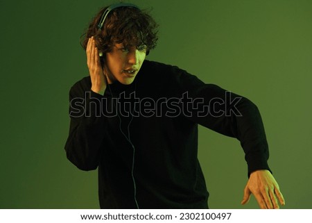 Man wearing headphones listening to music, dancing and singing with his eyes closed, DJ happiness and smile, hipster lifestyle, portrait green background mixed neon light, copy space