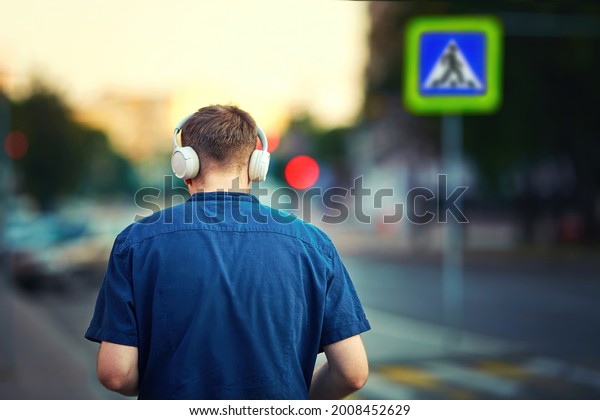 Man wearing headphones while walking on city\
street, pedestrian sign on background. Man listening to music\
approaches pedestrian crossing. Injuries, deaths rise for\
pedestrians wearing\
headphones