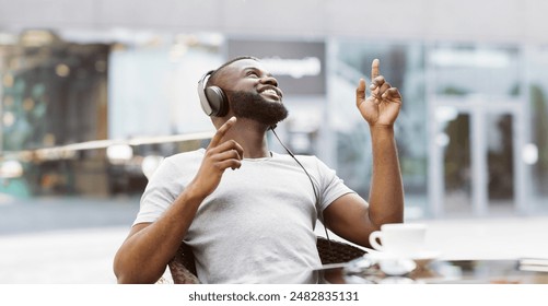 A man wearing headphones and a white t-shirt enjoys a sunny day outside by dancing to music. - Powered by Shutterstock