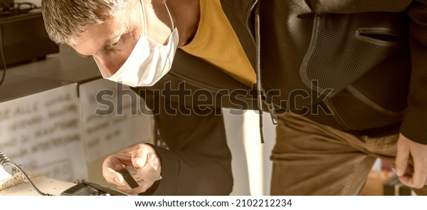 Man\
wearing health mask paying with card in a\
shop.