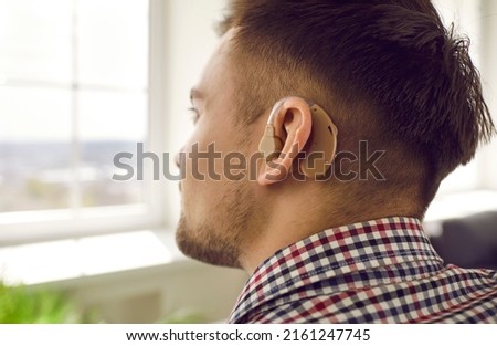 Man wearing hearing aid. Young hearing impaired patient wearing small comfortable digital or analog behind ear device. Close up side back view of man's head. Audiology and deafness treatment concept