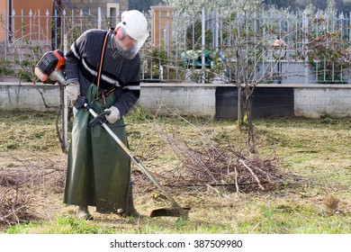 Man Wearing Helmet And Ear Protectors Mowing Grass In The Backyard With Petrol Hedge Trimmer