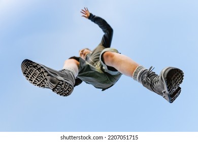 Man Wearing Hiking Boots And Bermuda Jumping Over, Seen From Under, With Uniform Blue Sky In The Background