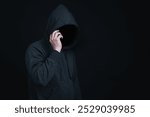 Man wearing hoodie is making phone call in dark background in concept of criminal or hacker try to lure or scam victim.