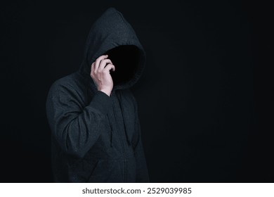 Man wearing hoodie is making phone call in dark background in concept of criminal or hacker try to lure or scam victim. - Powered by Shutterstock