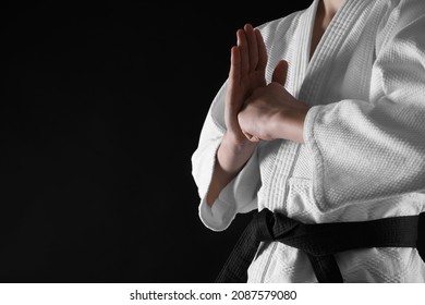Man wearing keikogi and black belt on dark background, closeup with space for text. Martial arts uniform