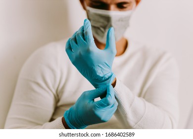 Man Wearing Latex Gloves and face mask indoors. Caucasian male using medical gloves while working at home during quarantine for virus prevention.
