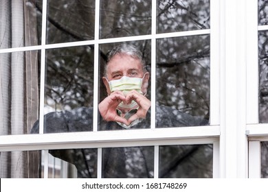 Mann mit Maske, der Herzsymbol mit Händen am Fenster macht