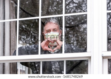 Man wearing mask making heart symbol with hands at the window