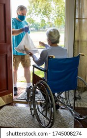 A man wearing a mask working with a church group or other benevolent organization brings some groceries to an elderly woman in a wheelchair. - Shutterstock ID 1745008274