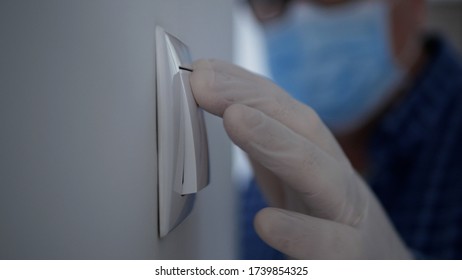 Man Wearing Medical Mask And Protection Gloves Enter In The Office Room Turning On The Light From The Switch On The Wall
