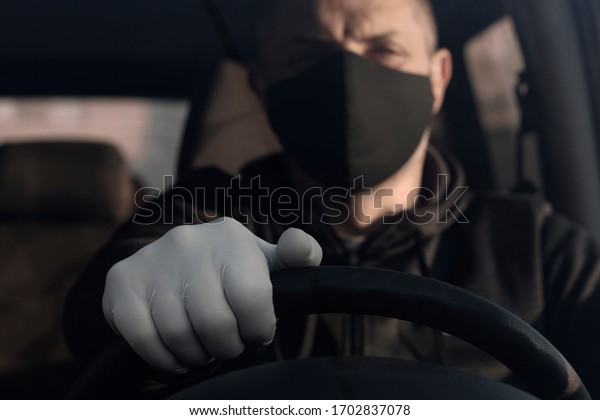 Man wearing medical\
protective gloves driving a car. A man driving a car puts on a\
medical mask during an epidemic, a taxi driver in a mask,\
protection from the virus.