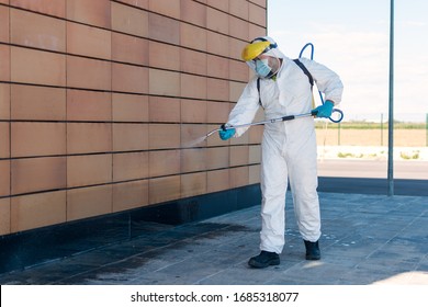 Man wearing an NBC personal protective equipment (ppe) suit, gloves, mask, and face shield, cleaning the streets with a backpack of pressurized spray disinfectant water to remove covid-19 coronavirus.