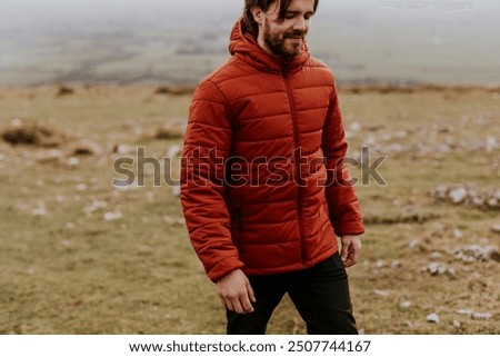 Man wearing orange puffer jacket, walking on hill