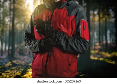Man wearing outdoor clothing, close up (hardshell waterproof jacket and softshell) standing with gloves on hands  - exploring and adventure concept. Forest in background