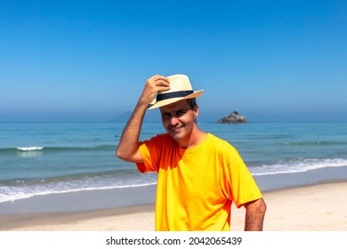 Man Wearing Panama Hat In An Orange T-shirt On The Beach, Smiling At The Camera