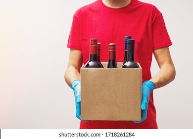 Man Wearing Protective Gloves Holding Box With Bottles Of Wine. Safe Online Wine Store Delivery During Quarantine.