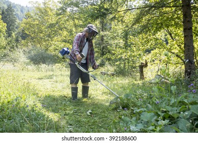 Man Wearing Protective Helmet With Goggles To Shield His Eyes While Trimming The Lawn With Weed Eater Surrounded With Green Trees.