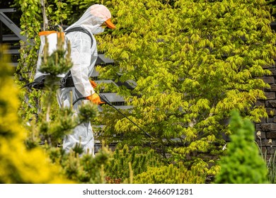 A man wearing a protective suit is spraying pesticide on a tree to control pests and diseases, ensuring the trees health and productivity. - Powered by Shutterstock