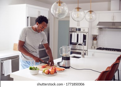 Man Wearing Pyjamas Standing In Kitchen Chopping Fruit And Vegetables For Fresh Smoothie - Powered by Shutterstock