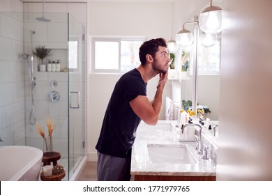 Man Wearing Pyjamas Standing At Sink Putting On Moisturizer In Bathroom