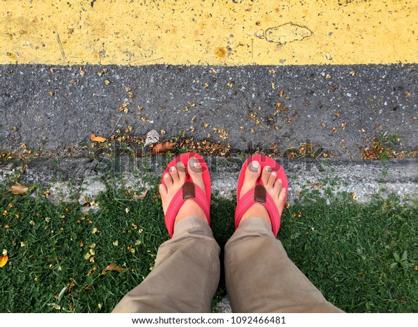 A man wearing red flip flops standing on the edge\
of a road divider