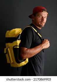 Man Wearing Red Hat Surfer With Yellow Waterproof Backpack. Dark Background.