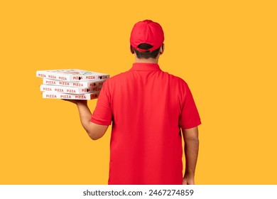 A man wearing a red uniform is standing, holding a box of pizza. The man appears to be delivering the pizza to a customer. The box is prominently displayed in his hands. - Powered by Shutterstock