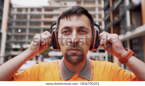 Man wearing safety equipment hearing protection.\
Worker wearing noise cancelling ear defenders or ear muffs.\
Construction builder puts on protect ears with headphones. Taking\
care safety during work.