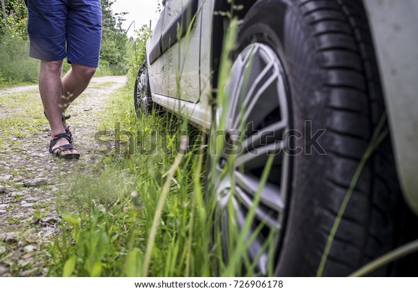 Man wearing\
shorts and sandals suitable to the car that is parked on the\
roadside near the forest, summer\
day.