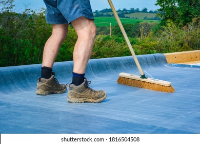 A Man Wearing Steel Toe Cap Work Boots Sweeping A Roof On A Construction Site