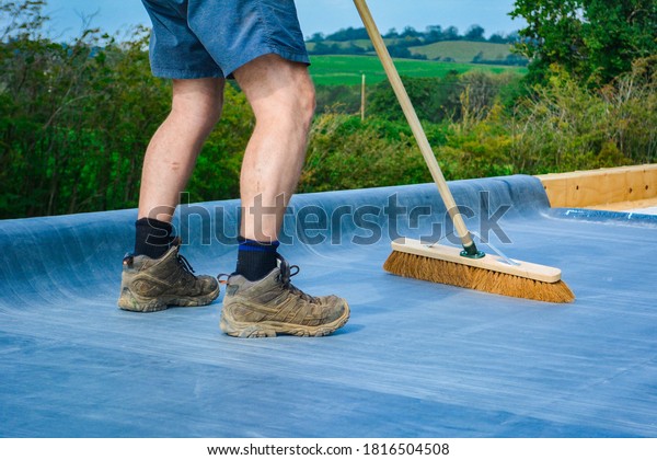 A man wearing steel toe cap work boots\
sweeping a roof on a construction\
site