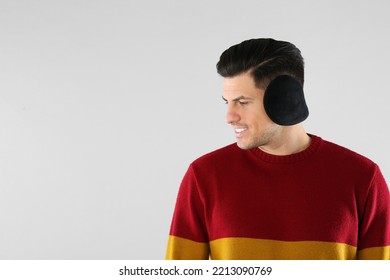 Man Wearing Stylish Earmuffs On Light Background. Space For Text