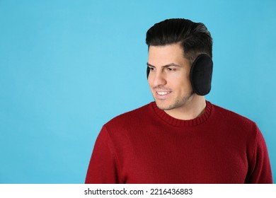 Man Wearing Stylish Earmuffs On Light Blue Background. Space For Text