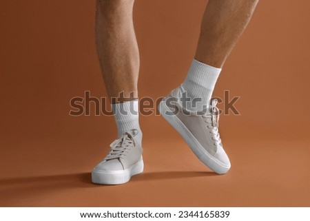 Man wearing stylish sneakers on brown background, closeup