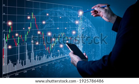 A man wearing a suit on his left hand holding a cell phone His right hand poked a pencil on a fast-growing stock chart. Globe background and blurred lights