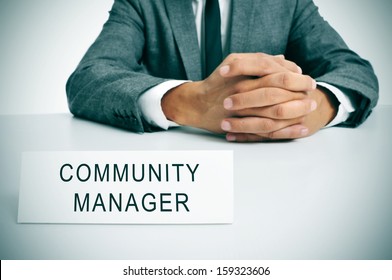 A Man Wearing A Suit Sitting In A Desk With A Signboard In Front Of Him With The Sentence Community Manager Written In It