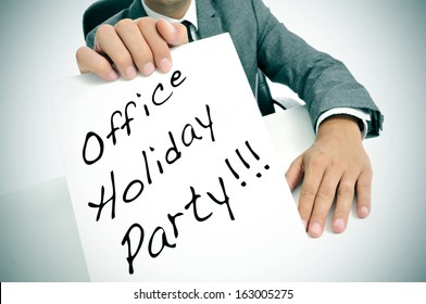 A Man Wearing A Suit Sitting In A Desk Holding A Signboard With The Text Office Holiday Party Written In It