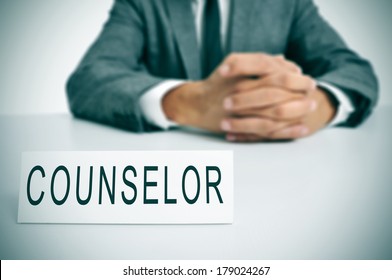 A Man Wearing A Suit Sitting In A Desk With A Desktop Nameplate In Front Of Him With The Word Counselor