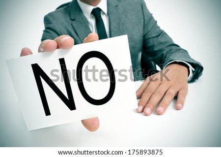 man wearing a suit sitting in a table showing a signboard with the word no written in it